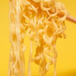 Authentic Cuisine - Crop anonymous person holding instant noodles with bamboo chopsticks against yellow background