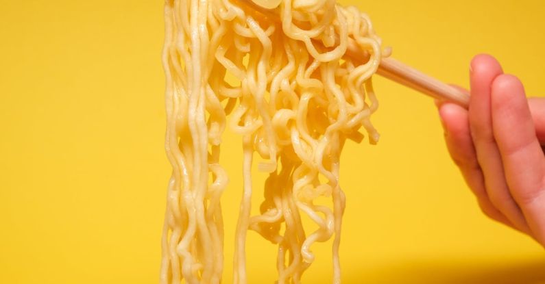 Authentic Cuisine - Crop anonymous person holding instant noodles with bamboo chopsticks against yellow background